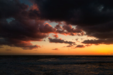 Naklejka na ściany i meble Cloudy sunset at the stormy sea.
