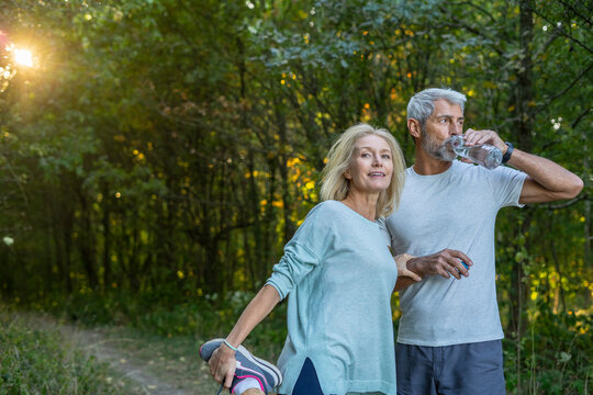 Smiling mature couple exercising and drinking water in forest