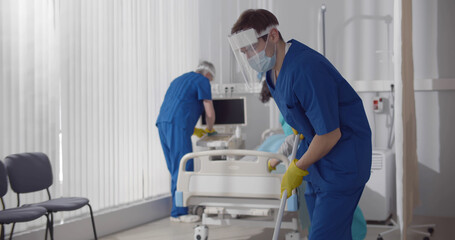 Fototapeta na wymiar Janitors in scrubs and safety mask cleaning hospital room