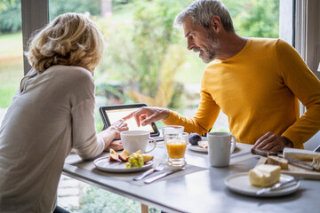 Mature couple using digital tablet while having breakfast at home