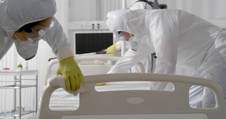 Team in protective suit and mask disinfecting furniture in hospital room from corona virus