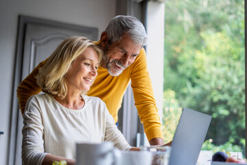 Smiling mature couple using laptop at home