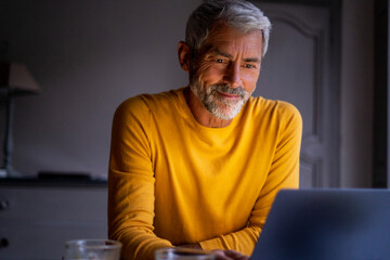 Smiling mature man using laptop at home