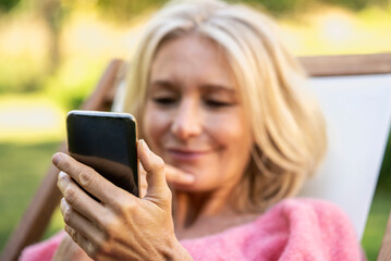 Close-up of smiling mature woman using smartphone while sitting on deckchair