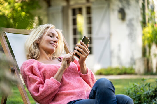 Smiling Mature Woman Using Smartphone While Sitting On Deckchair