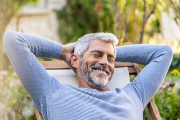 Smiling mature man with hands behind head sitting on deckchair