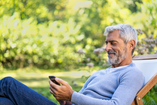 Smiling mature man using smartphone while sitting on deckchair
