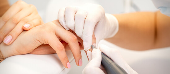 Obraz na płótnie Canvas Manicure master applying electric nail file machine removing old nail polish on fingernails in a nail salon