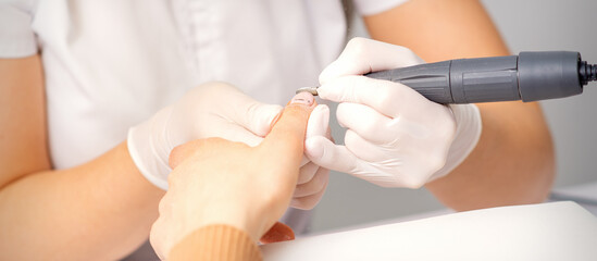 Manicure master applying electric nail file machine removing old nail polish on fingernails in a nail salon