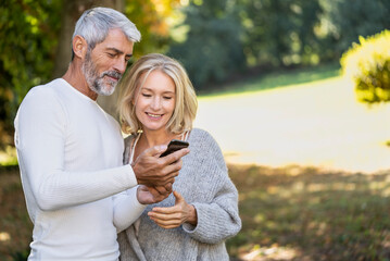 Smiling mature couple using smartphone in backyard