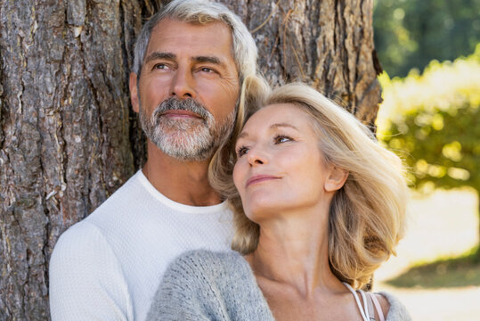 Thoughtful mature couple leaning on tree trunk