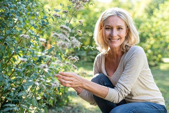 Portrait of smiling mature woman touching plant in backyard