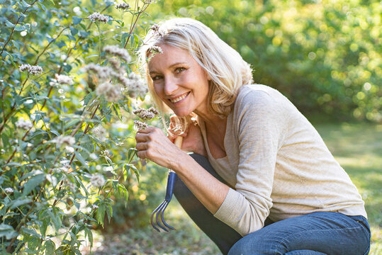 Portrait of smiling mature woman smelling flowers in backyard