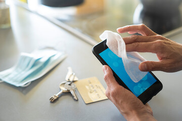 Close-up of woman's hands disinfecting smart phone with wet wipe at home