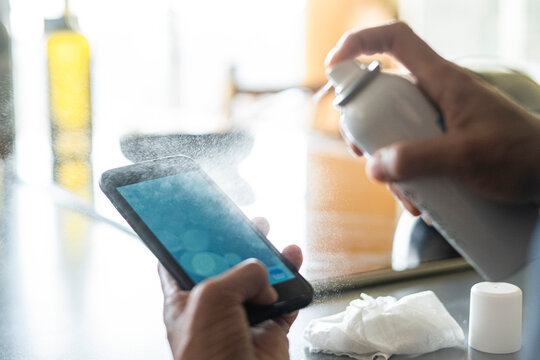 Close-up of woman's hands spraying disinfectant on smartphone at home