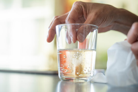 Close-up Of Woman's Hand Dropping Pill In Glass Of Water