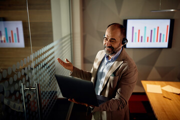 Happy businessman using laptop and talking during online video meeting at corporate office.