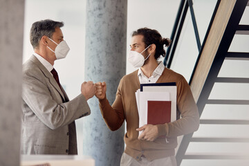 Business co-workers fist bumping while greeting in hallway during coronavirus pandemic.