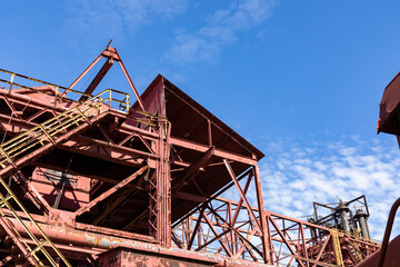 Abandoned industrial site, stairs and open walkways with rusted metal and peeling paint against a beautiful blue sky, horizontal aspect