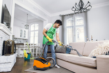 Fototapeta na wymiar Indian male cleaner cleaning sofa with modern vacuum cleaner