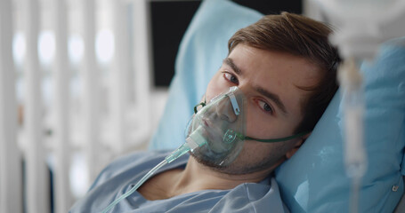 Young attractive man with oxygen mask looking sad and worried lying at hospital bed