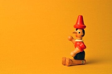 Wooden puppet depicting Pinocchio sitting on a yellow background