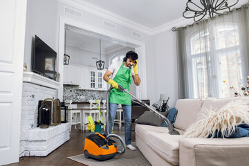 Fototapeta na wymiar Indian man in headphones vacuuming couch at bright room