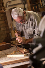 Experienced senior carpenter working in his workshop.Carving and working with chisel.