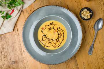 Soup cream of pumpkin on grey plate with bread croutons on wooden table