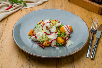 salad with pumpkin, cheese and herbs on grey plate on wooden table