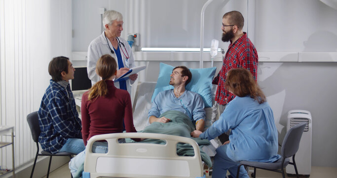 Family and friends visiting patient in hospital ward and talking with doctor.