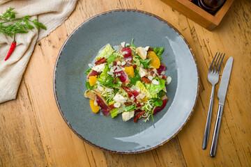 salad with orange, Parma ham and cheese on grey plate on wooden table