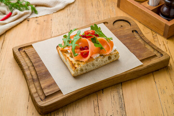 Bruschetta with salmon, cheese, aragula and cranberries on wooden board