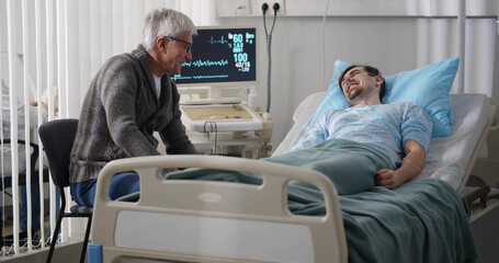 Aged man visiting young sick son in hospital ward