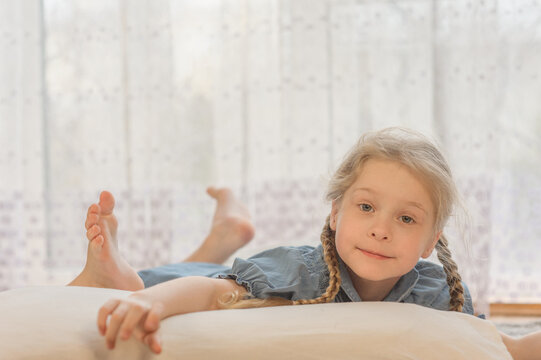 a little girl with two pigtails of blond hair lies on her stomach on the floor of the house and shows her tongue