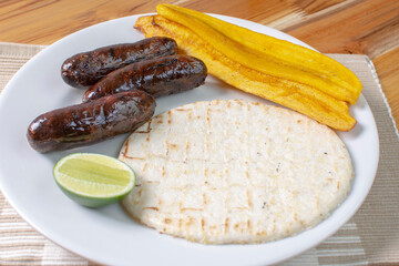 Arepa with blood sausage, fried banana, lemon, traditional Colombian food, on wooden background