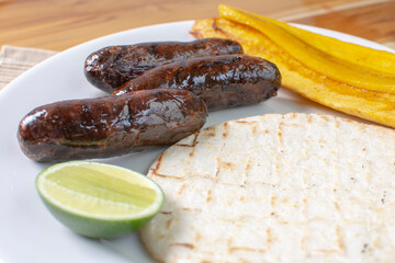 Arepa with blood sausage, fried banana, lemon, traditional Colombian food, on wooden background
