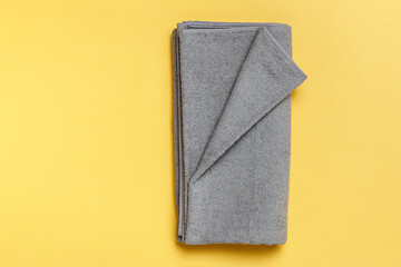 Close-up on a gray folded towel against a yellow background. Flat lay top view copy space.