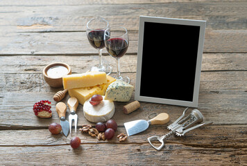 Empty mockup black frame near the cheese board and red wine on the rustic wooden table.
