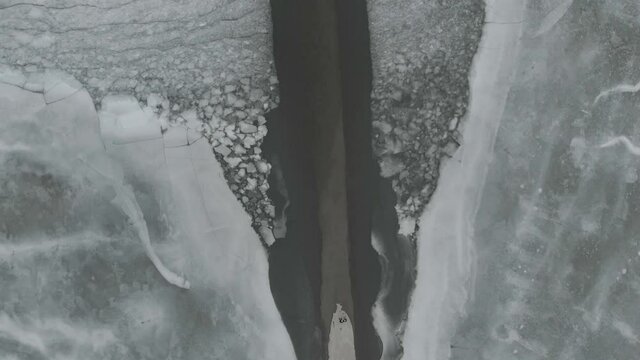 Top Down Drone Shot Over Melting Lake Ice With Underwater Road With Two People On The End Of The Road 4K