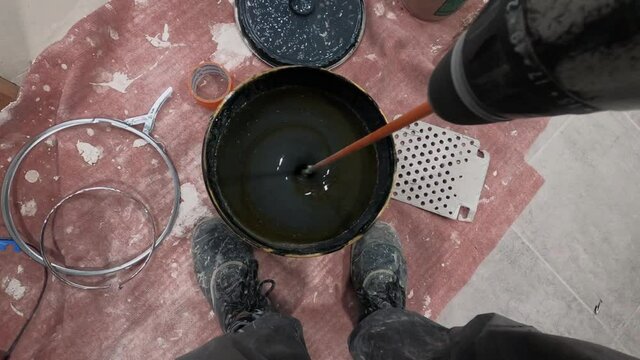 The Process Of Mixing black paint and hardener in a Bucket with a driller