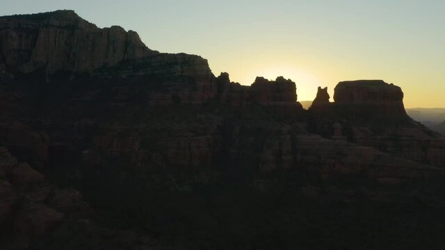 The morning sun silhouettes Bear Mountain and surrounding rock formations near Sedona, Arizona at dawn. An aerial shot trucking from left to right.