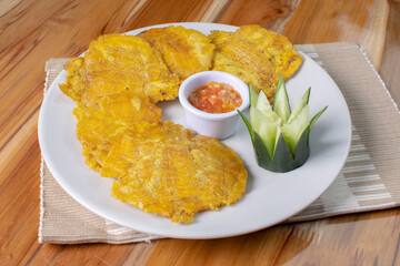 Patacon with stew, fried banana, decorated in white plate on wooden background