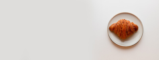 Freshly baked croissant with caramel filling on plate on grey background. Minimal composition. Flat lay, top view