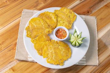 Patacon with stew, fried banana, decorated in white plate on wooden background