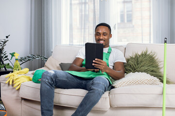 Smiling afro-american janitor sitting on couch with tablet