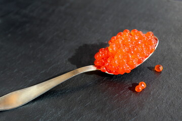 Spoon with red caviar on a black background