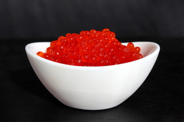 Red caviar in a white small plate on a black background