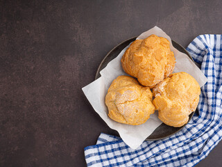 Top view of choux cream on a plate and cloth placed on a dark brown background. Space for text. Concept of relaxation