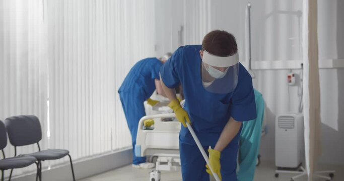 Janitors in scrubs and safety mask cleaning hospital room